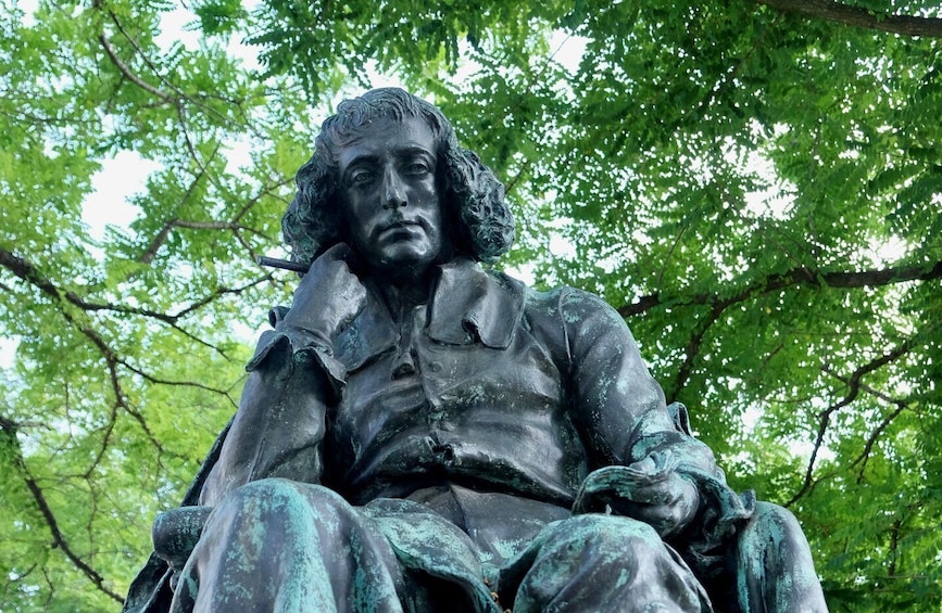 A bronze statue of a seated man with a contemplative expression, surrounded by lush green foliage. 5