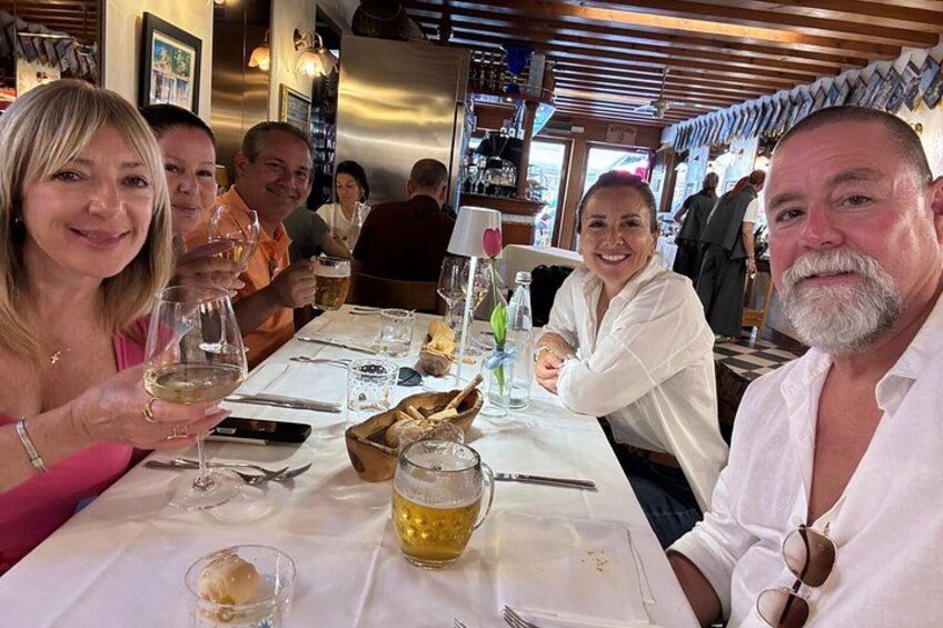 Un grupo de personas sentadas en una mesa de restaurante, con copas de vino y una jarra de cerveza. 4
