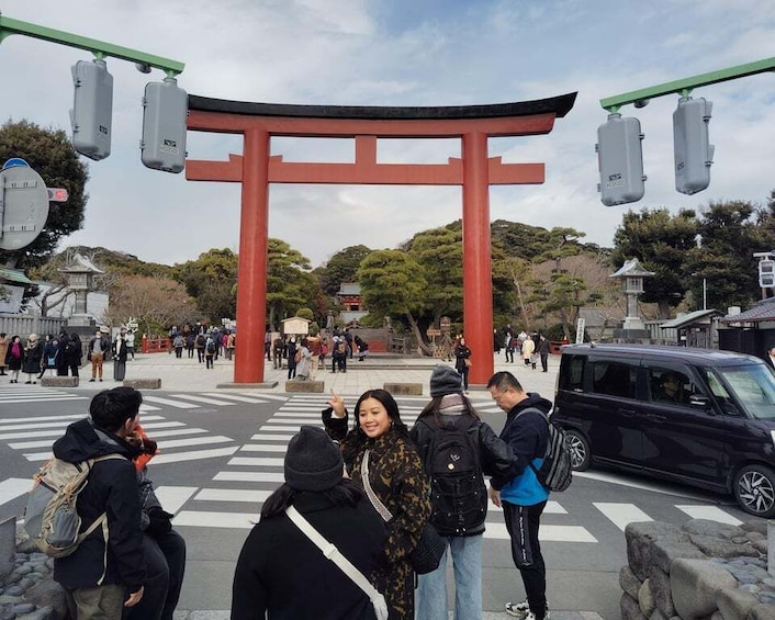 A red torii gate with traffic lights above it, surrounded by people and vehicles. 1