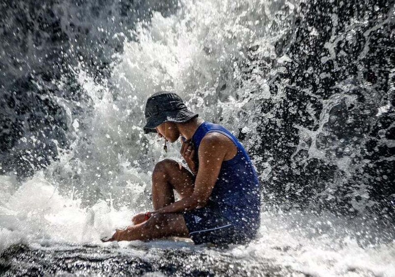 A person sitting on a surfboard in a waterfall. 4