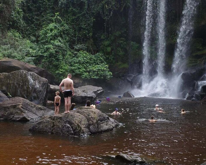 A waterfall, rocky terrain, and people swimming in a natural pool. 2