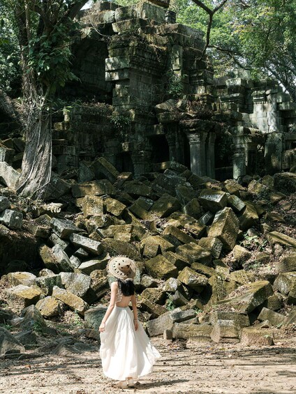 A person in a white dress walking away from a stone structure surrounded by trees. 1