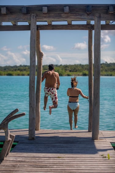 A wooden pier extending into a turquoise sea with a man and a woman jumping off into the water. 3