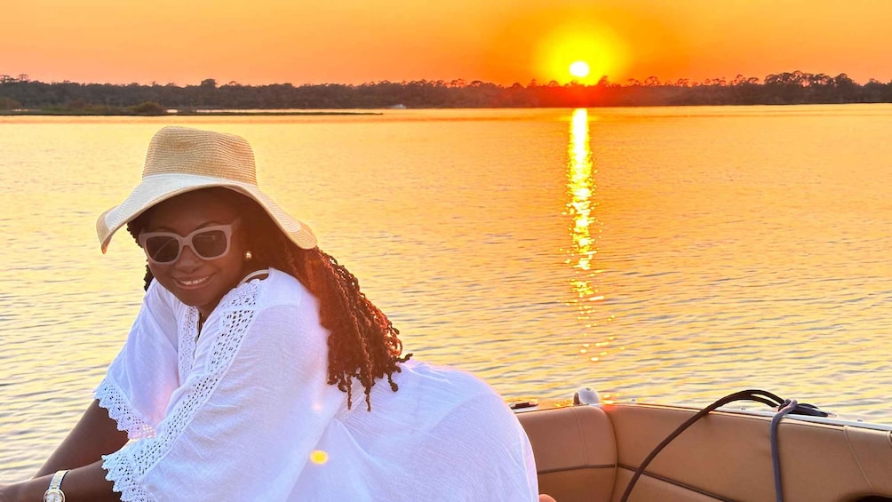 A person in a white dress and hat sitting on a boat with a sunset in the background. 3