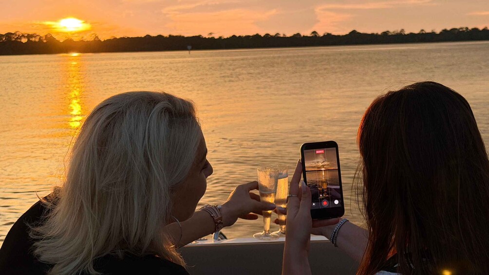 Two people at a lakeside table during sunset, one holding a smartphone. 4