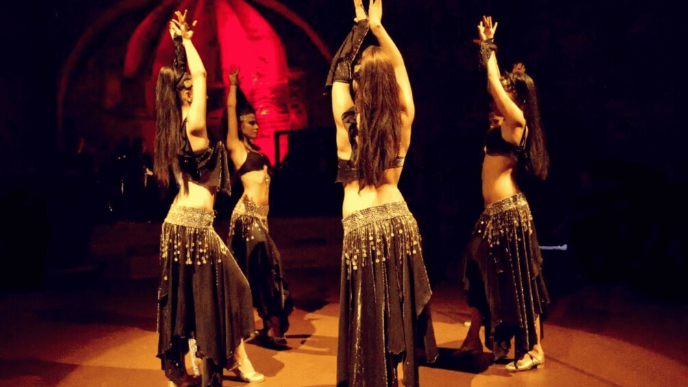 A group of dancers in black costumes with sequins, performing on a stage with a red backdrop. 1