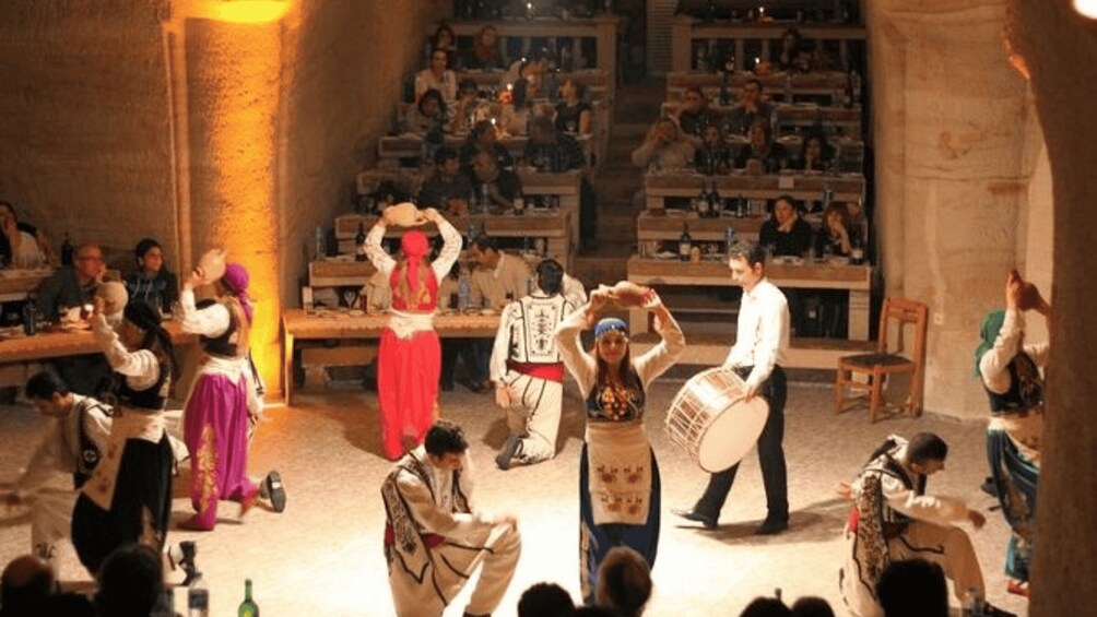 A traditional dance performance in a dimly lit venue with an audience seated in the background. 5