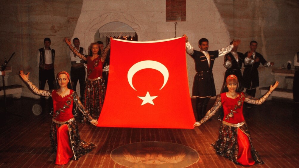 A group of people in traditional costumes holding a large Turkish flag. 3