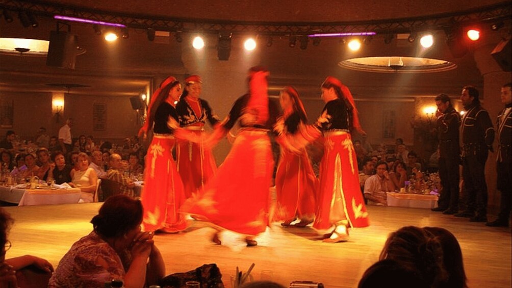A group performing a dance on stage with an audience seated in a dimly lit room. 4