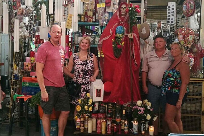 A group of people posing in a store with a large skeleton figure and various bottles and flowers on display. 2
