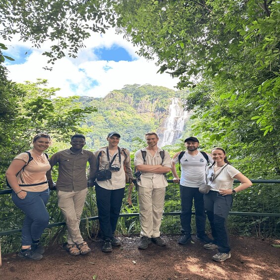 A group of people standing by a waterfall in a forested area. 5