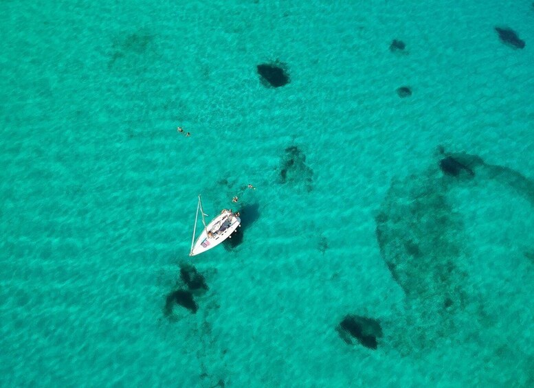 A small boat anchored in clear turquoise waters with visible coral formations. 2