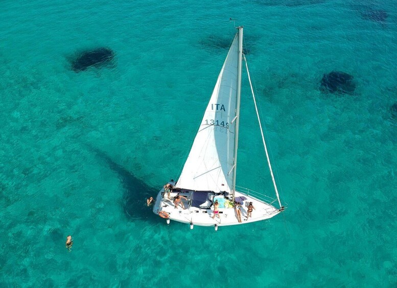 A sailboat with people on board in clear turquoise water. 3