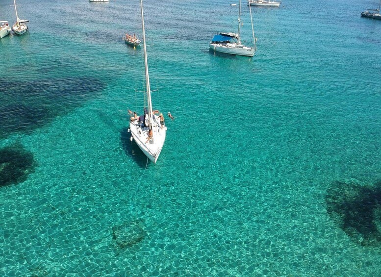 A sailboat anchored in clear turquoise waters with other boats in the background. 1