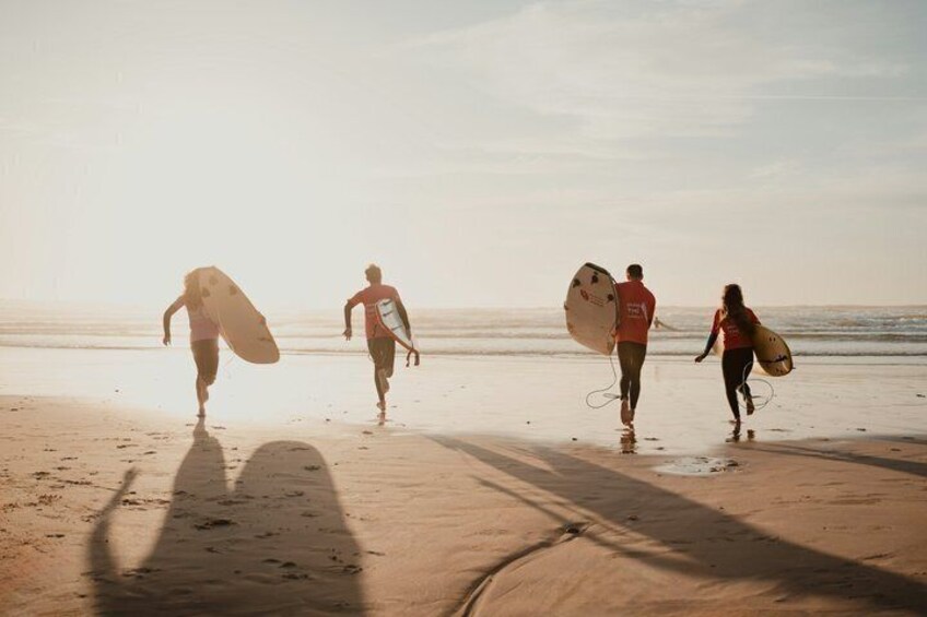 Four people walking on a beach with surfboards. 4