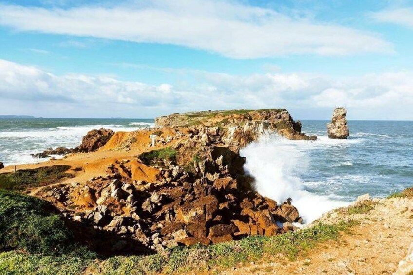 A coastal landscape with rocky cliffs, waves crashing against the shore, and a prominent rock formation in the distance. 5