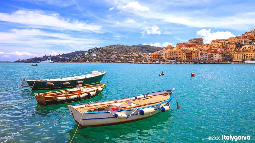 A coastal town with boats docked in clear blue waters, a lighthouse in the distance, and colorful buildings on the hillside. 1