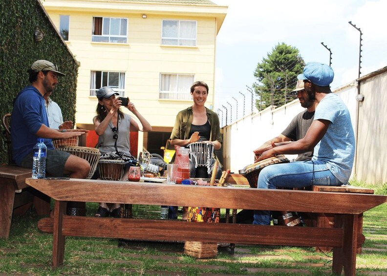 A group of people sitting around a wooden table outdoors with musical instruments and a water bottle. 3