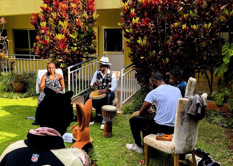 A group of people playing drums outdoors, with a building and trees in the background. 2
