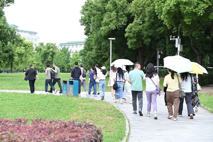 A group of people walking on a paved path in a park with trees and a building in the background. 2