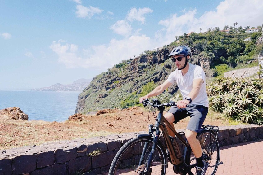 A person riding a bicycle on a paved path by the sea. 1