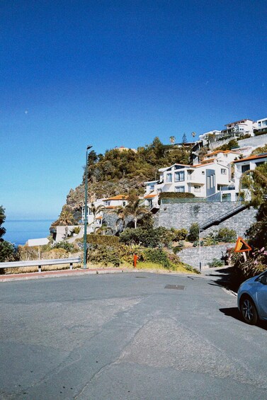 A coastal road with houses on a hillside, a clear blue sky, and the ocean in the background. 3