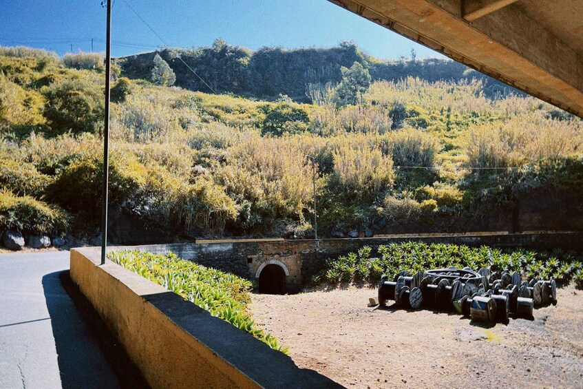 A concrete structure with a dirt ground, a stone bridge, and a hillside with vegetation. 2
