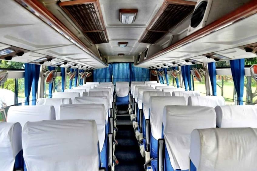 A train interior with rows of white-covered seats, blue curtains, and overhead fans. 3