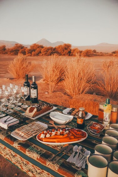 A desert picnic setup with wine bottles, glasses, bread, and snacks. 3