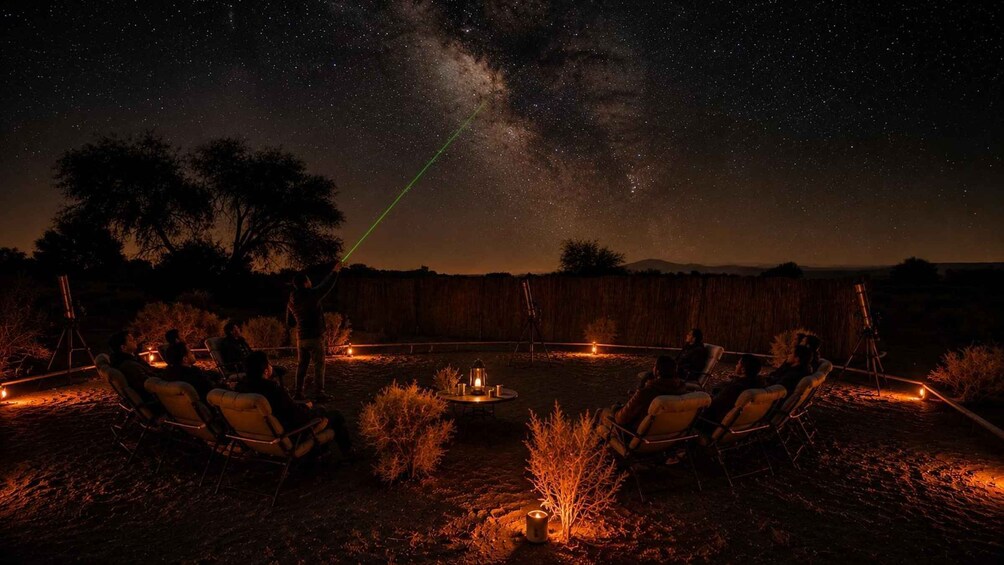 A night sky with stars and the Milky Way, a campfire, and people sitting on chairs in a backyard. 4