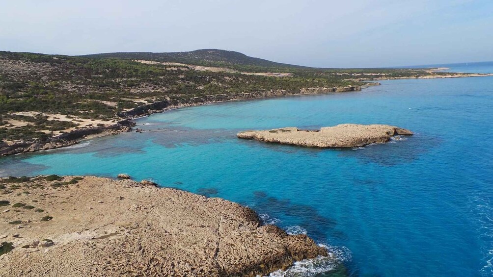 A coastal landscape with a rocky shoreline, clear blue waters, and a small island. 3