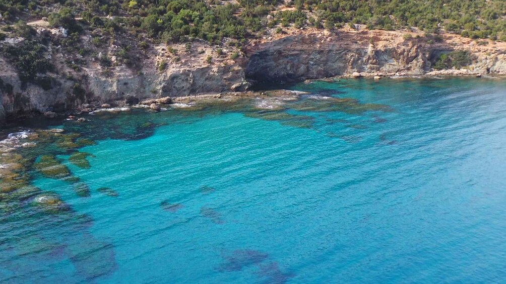 A coastal landscape with clear turquoise waters, rocky cliffs, and sparse vegetation. 4