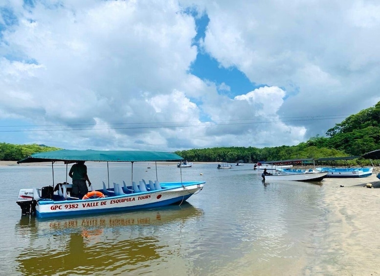 A boat named GPC 9382 VAVE DE ESQUIPULA TOURS on calm water with a cloudy sky and greenery in the background. 1