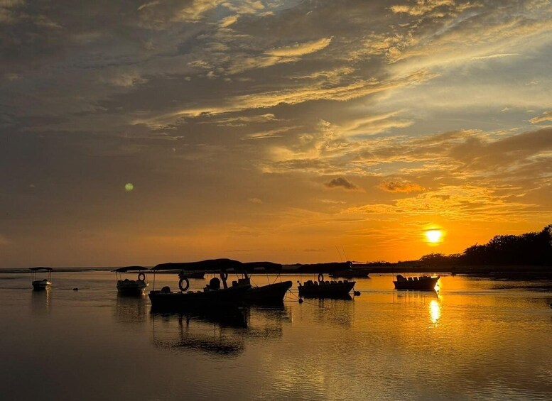 A sunset over a calm body of water with boats anchored. 1