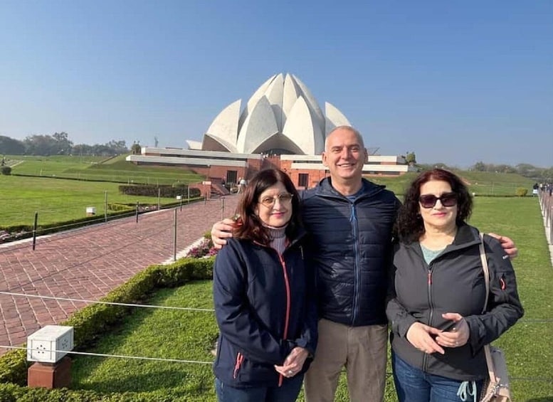 Three people standing in front of a large white lotus-shaped building with a brick pathway and green grass in the background. 1