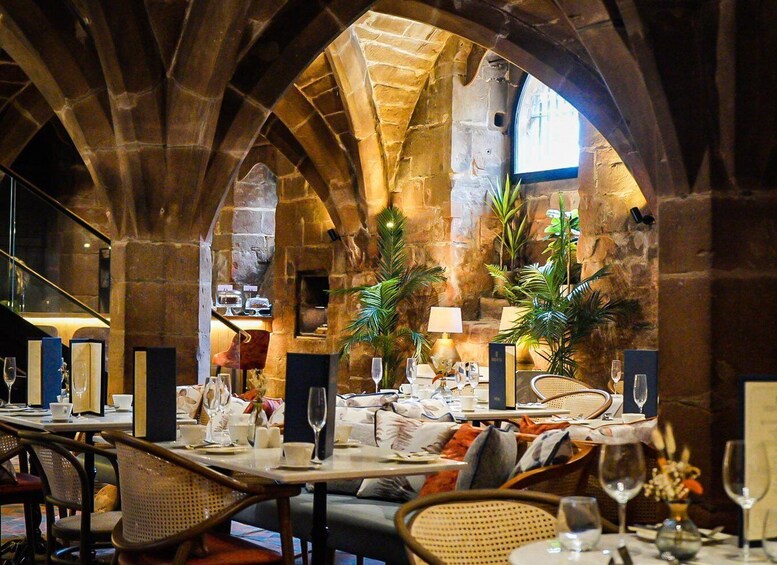 A restaurant with stone arches, tables set for dining, and potted plants. 2
