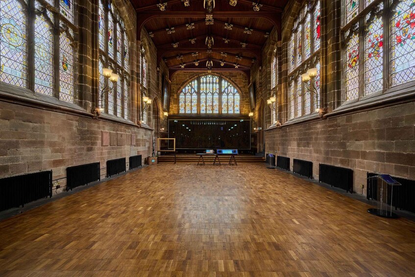 A large hall with wooden floors, high arched windows, and stone walls. 5