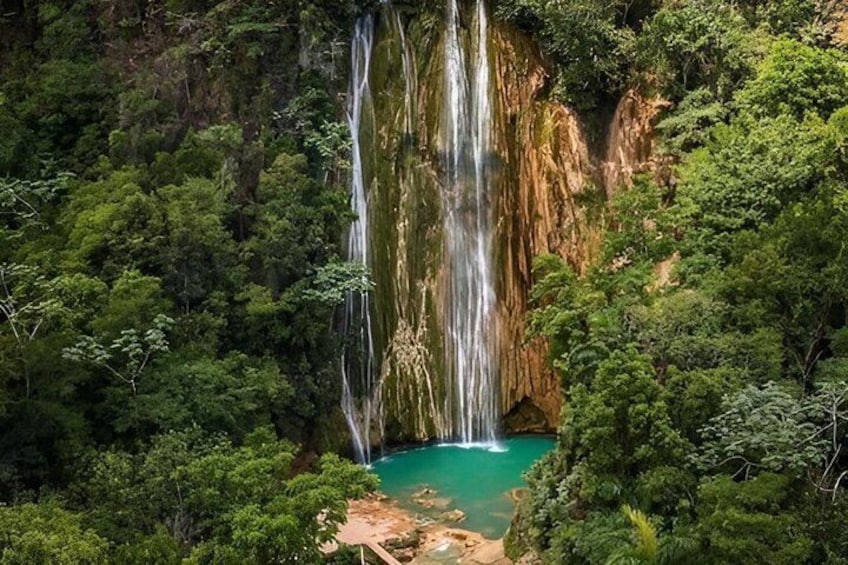 Een waterval stort neer in een turquoise poel, omringd door dicht bos. 3