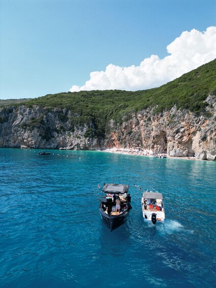 Two boats on a turquoise sea with a rocky coastline and a beach in the background. 3