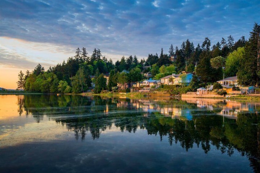 Un lac paisible où se reflètent les maisons et les arbres, entouré d’une zone boisée. 1