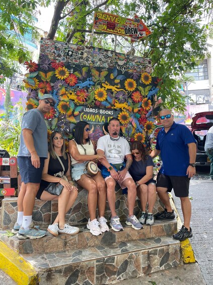 A group of people sitting on a stone bench with a colorful mural in the background. 3