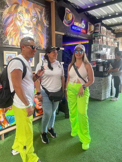 Three people standing in a cafe with a lion mural and a neon sign. 1
