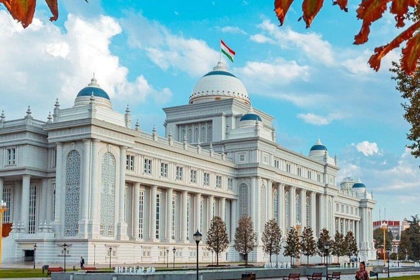 A large white building with domes and a flag, surrounded by trees and a clear sky. 1