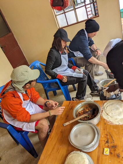 People preparing food at a table with a pot of stew and tortillas. 1