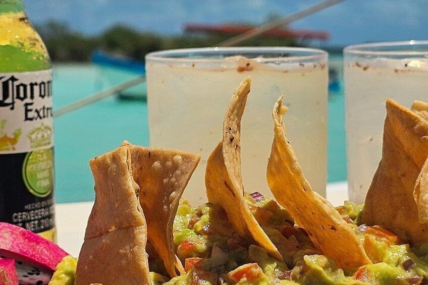 A poolside setting with a Corona beer bottle, two glasses of a light-colored beverage, and tortilla chips. 4