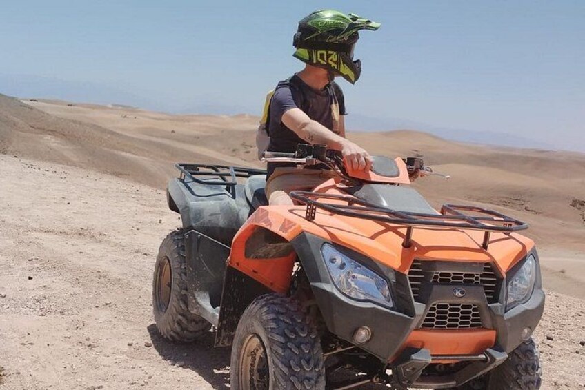 Une personne conduisant un quad orange sur un terrain sablonneux. 1