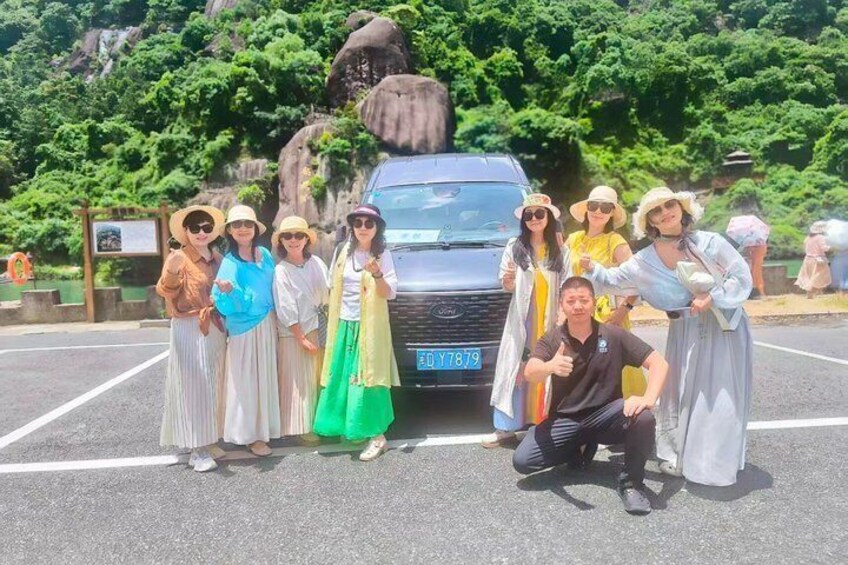 A group of people posing in a parking lot with a car and a large rock formation in the background. 4