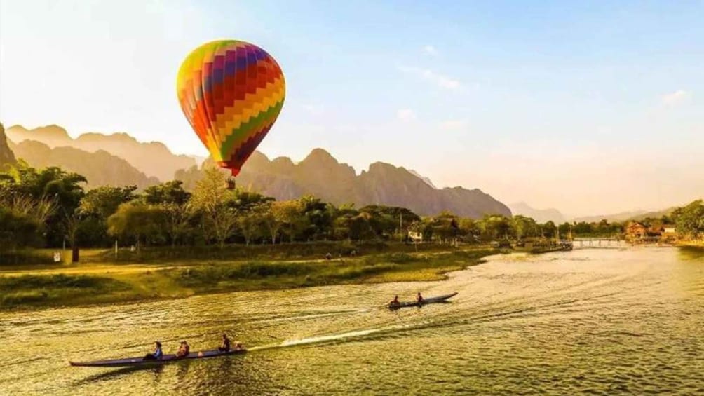 A hot air balloon over a river with people rowing boats. 5