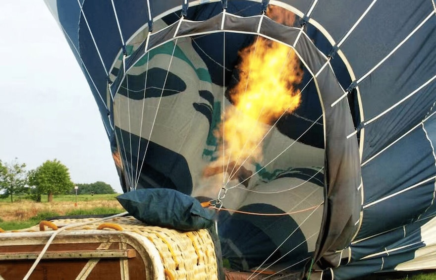 A hot air balloon with flames inside, a wicker basket, and a landscape with trees and grass. 3