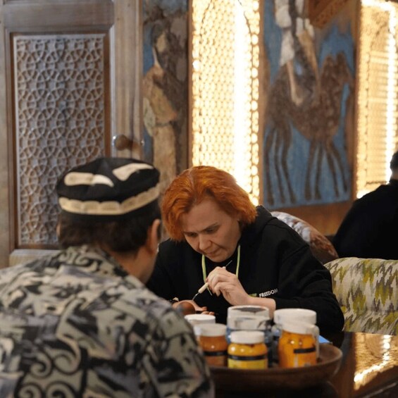 A person with red hair sitting at a table with jars of honey. 1